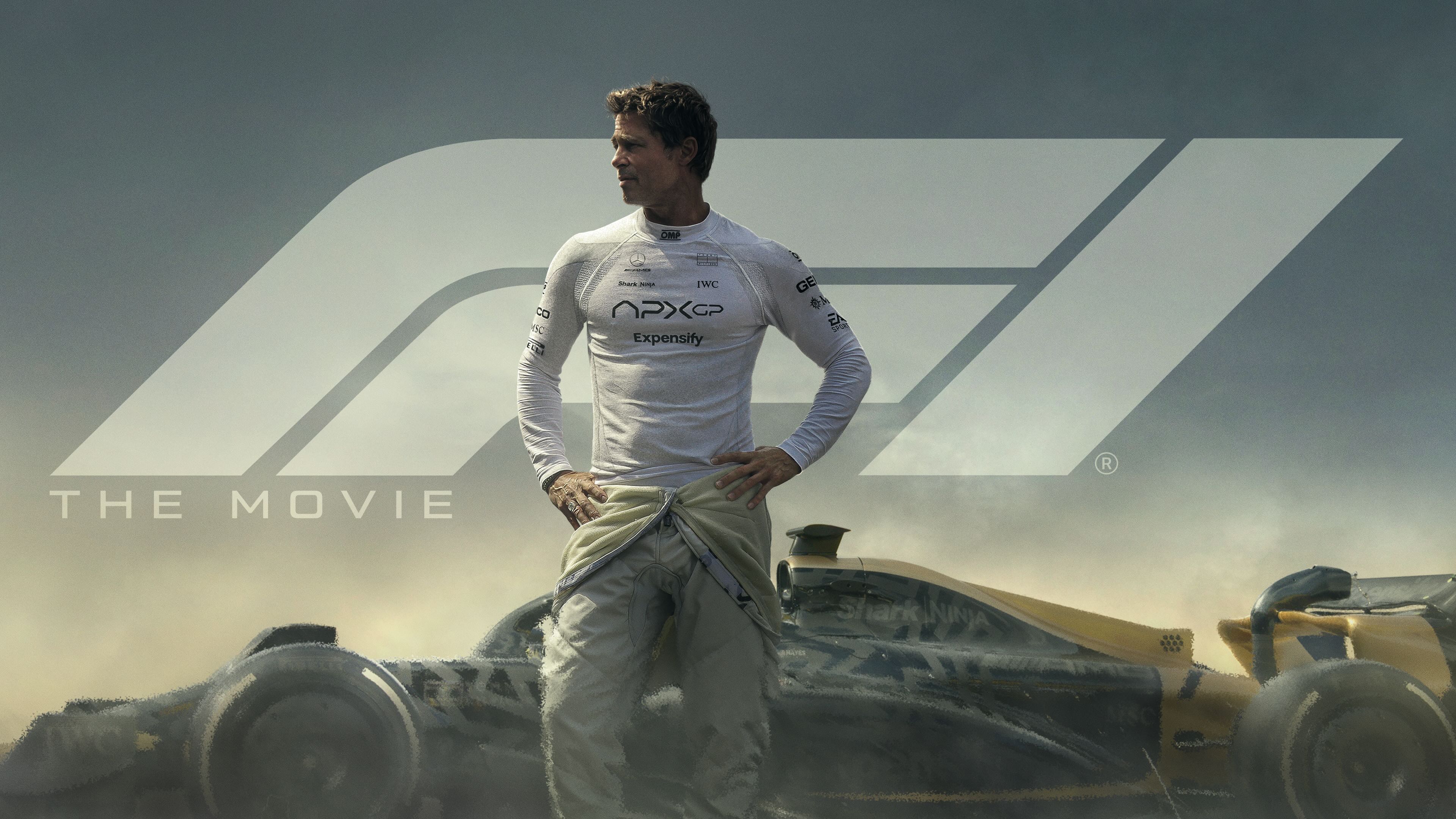 Brad Pitt as Sonny Hayes in a white racing suit stands before an APXGP Formula 1 car, with the F1 The Movie logo.