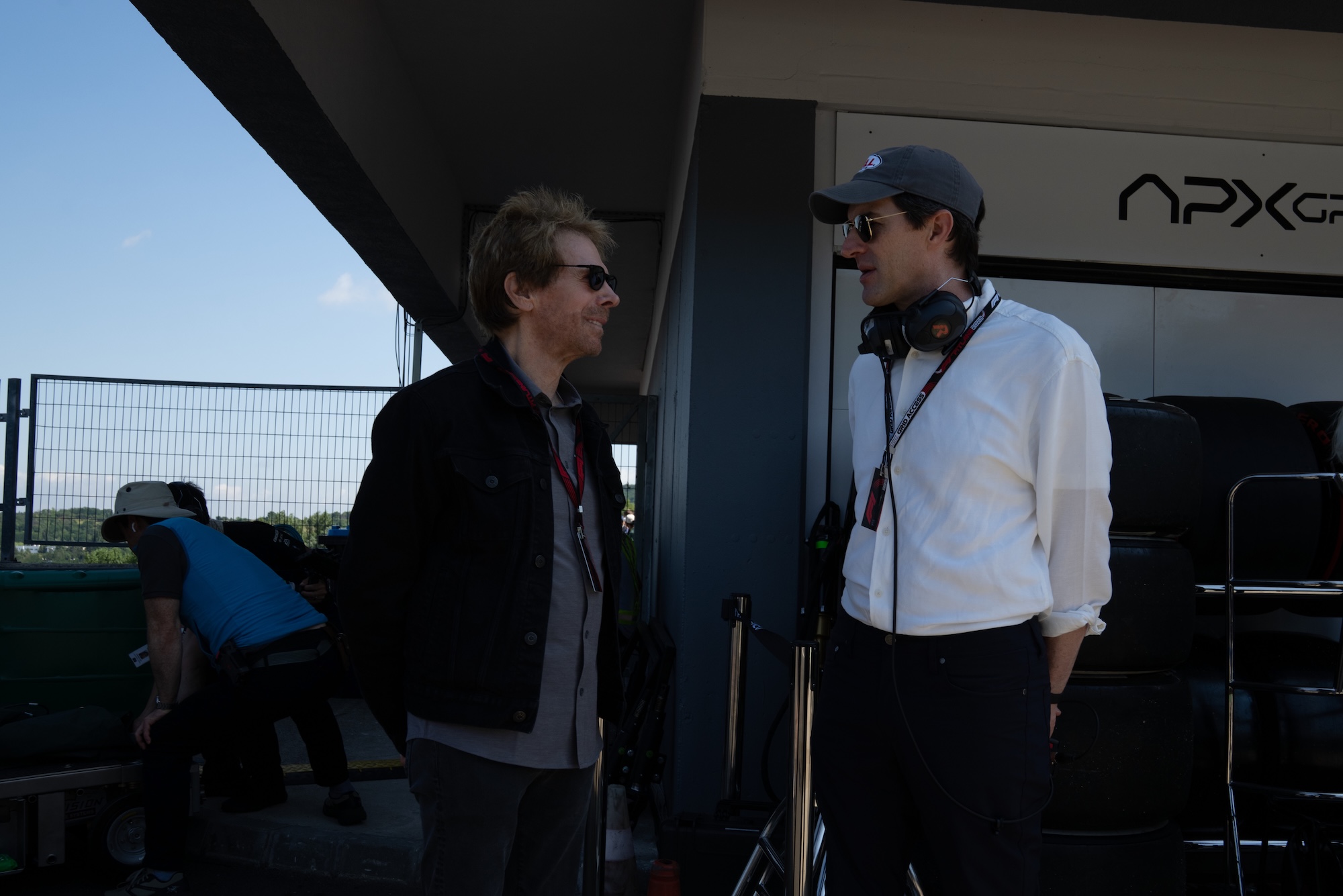 Producer Jerry Bruckheimer and director Joseph Kosinski converse in a pit lane area at a race track.
