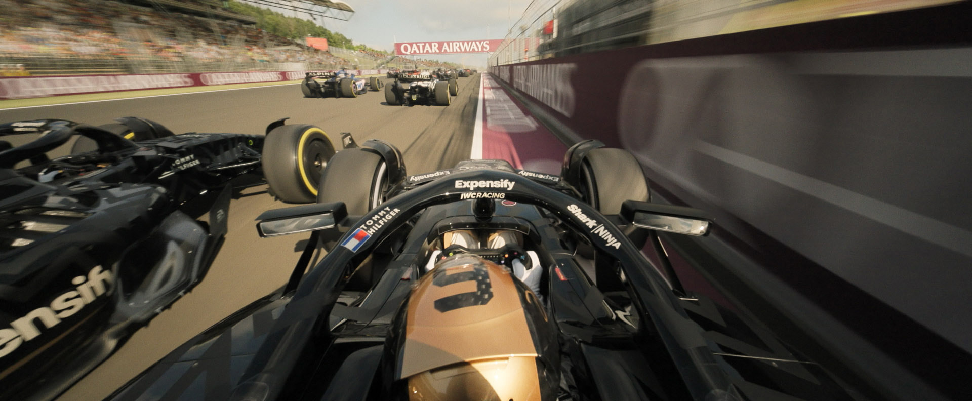 An onboard view of an APXGP Formula 1 car racing at full speed between another car and the track barrier