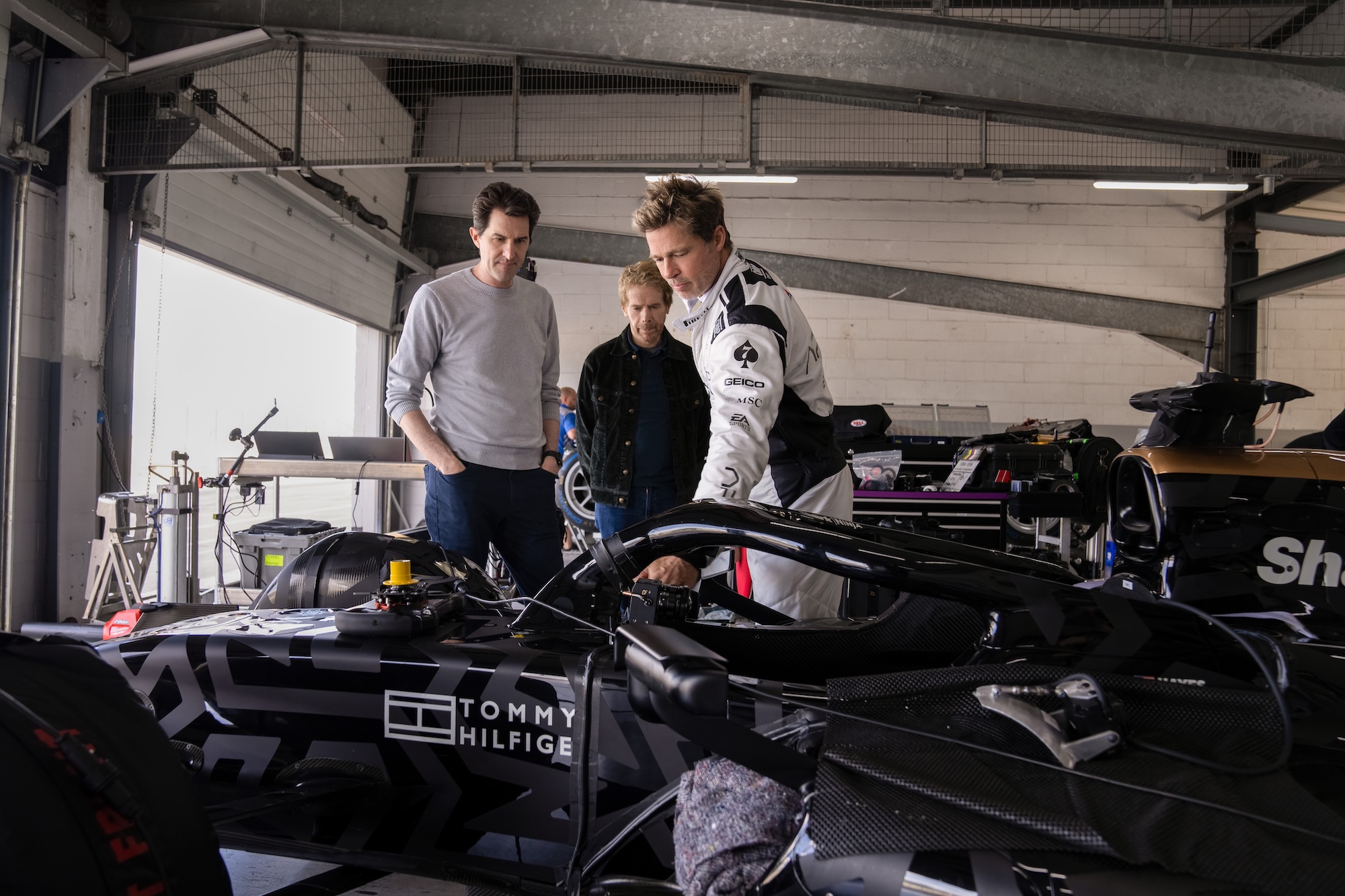 A behind-the-scenes view of director Joseph Kosinski, producer Jerry Bruckheimer, and Brad Pitt looking at a Formula 2 car used for racing scenes.